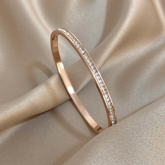 Maison Amara Aube rose gold bangle bracelet with a delicate row of sparkling crystals on a soft champagne silk fabric.