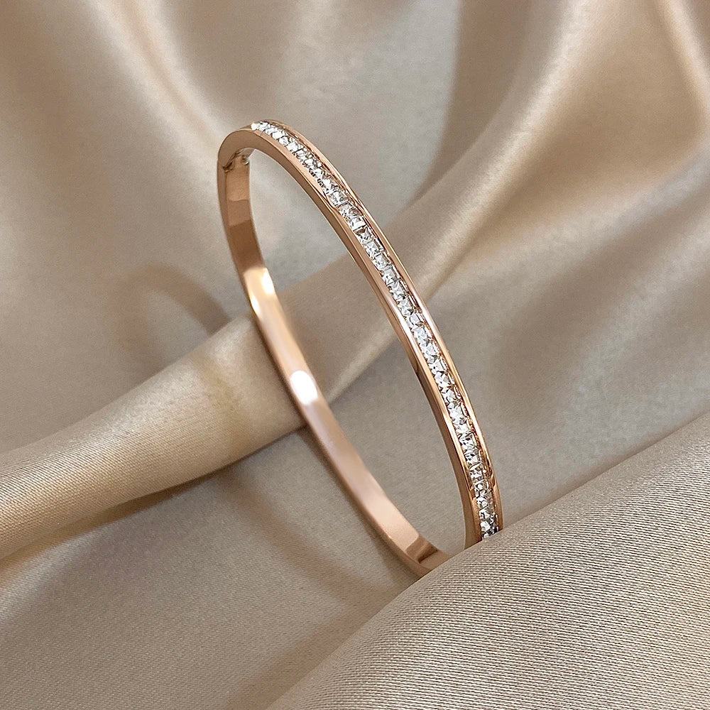 Maison Amara Aube rose gold bangle bracelet with a delicate row of sparkling crystals on a soft champagne silk fabric.